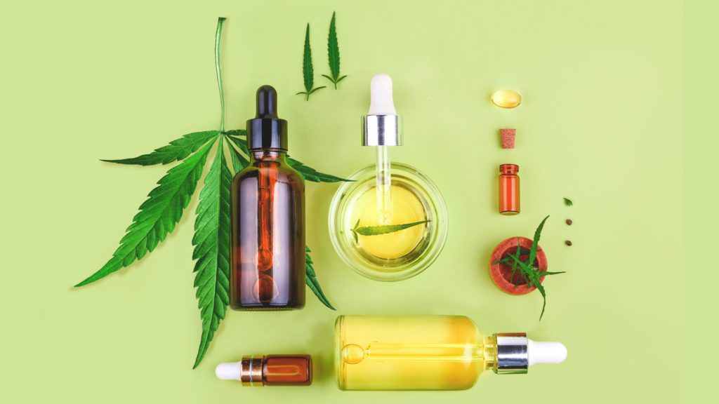 cbd oil bottles and cannabis leaf on a green table 