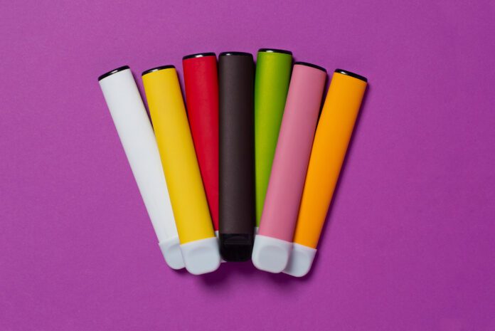 Set of colorful disposable electronic cigarettes on a purple background. The concept of modern smoking, vaping and nicotine. Top view
